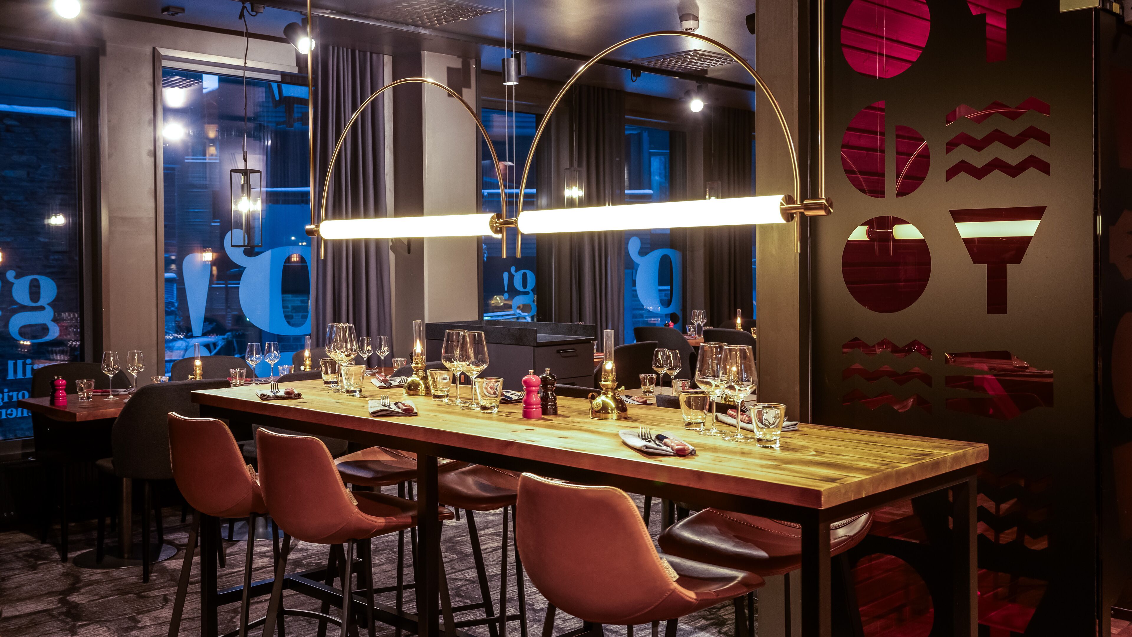 Een restaurant met een lange houten tafel, gedekt voor een maaltijd, meerdere wijnglazen en een modern interieur.