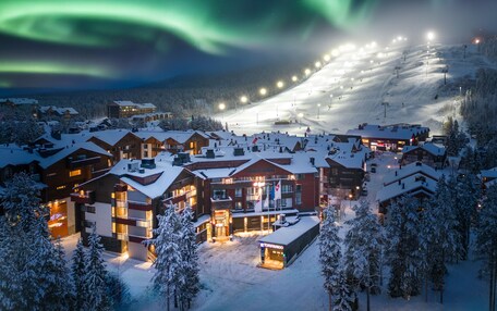 A snow-covered ski resort at night with illuminated buildings and a ski lift in operation.