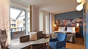 A modern hotel room with a sofa, a chair, a small table, and a bed with a headboard. There is a window with curtains, a wall with a painting, and a lamp on the bedside table. - Break Sokos Hotel Levi (Kittila)