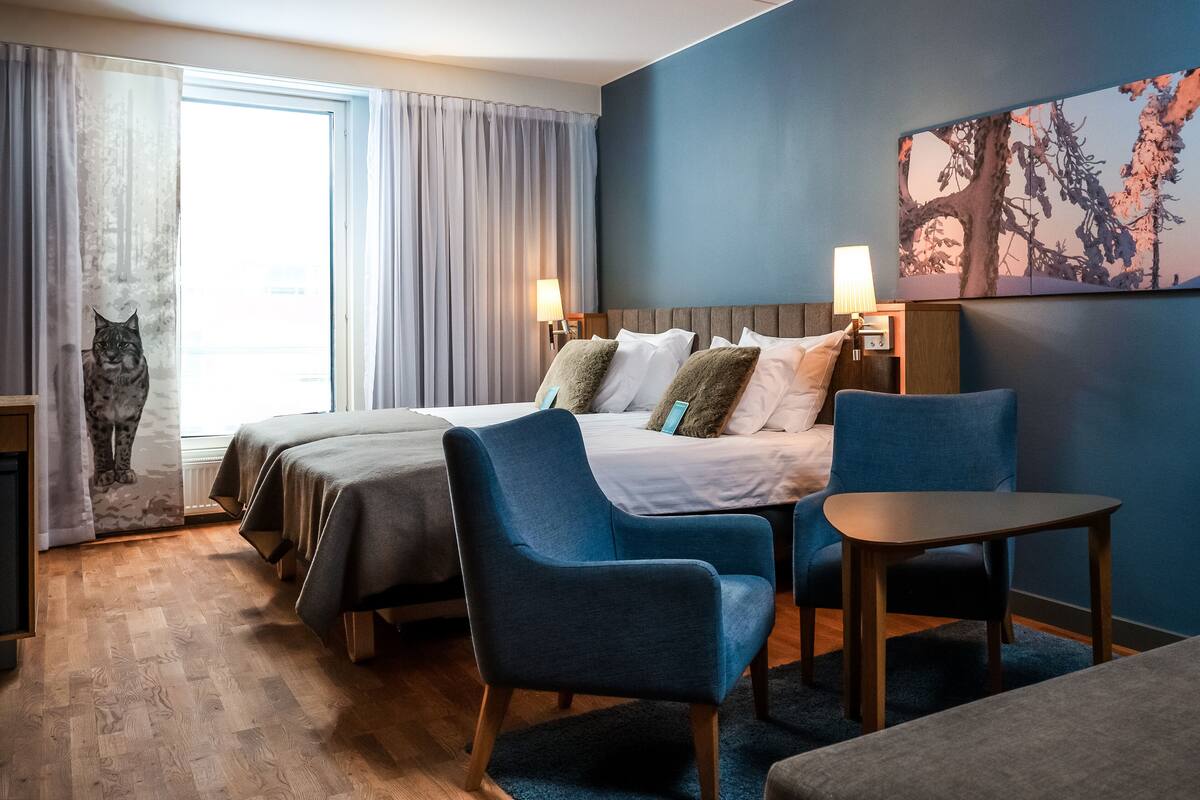 A hotel room with a large bed, two chairs, a small table, and a painting on the wall.