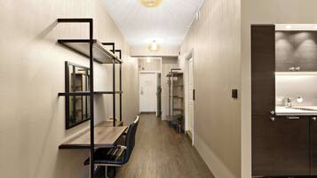 A hallway with a wooden floor, a built-in bench, a wall-mounted shelf, and a door leading to a bathroom.
