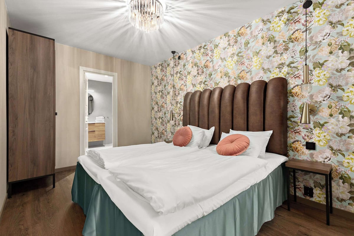 Un dormitorio con cama, armario de madera, papel tapiz floral y una araña.