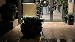La entrada del Hotel & Apartamentos Ole Bull, con fachada oscura, puerta de cristal y coronas navideñas.