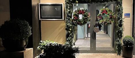 La entrada del Hotel & Apartamentos Ole Bull, con fachada oscura, puerta de cristal y coronas navideñas.