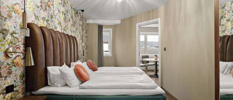 A hotel room with a large bed, a chandelier, floral wallpaper, and a view through an open door.