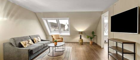 A modern living room with a sofa, armchair, coffee table, TV, and a large window.