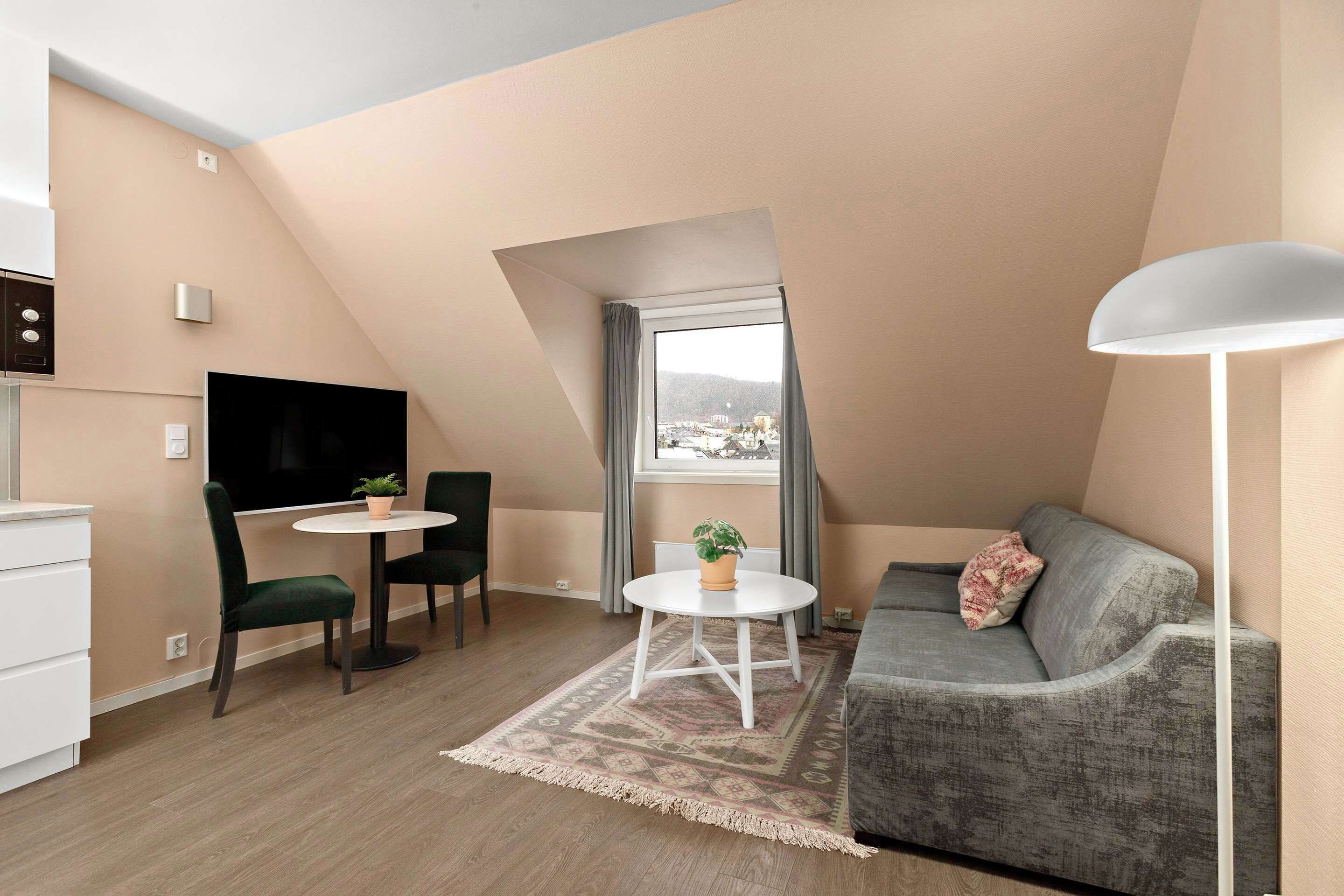 A modern apartment with a dining area, a sofa, a TV, and a view of a cityscape through a window.