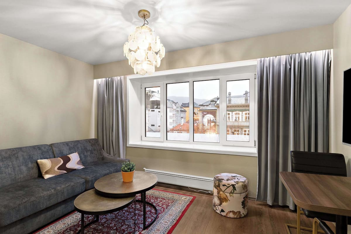 Una sala de estar moderna con sofá, mesa de centro, reposapiés y un amplio ventanal con cortinas.