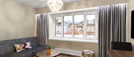 Una sala de estar moderna con sofá, mesa de centro, reposapiés y un amplio ventanal con cortinas.
