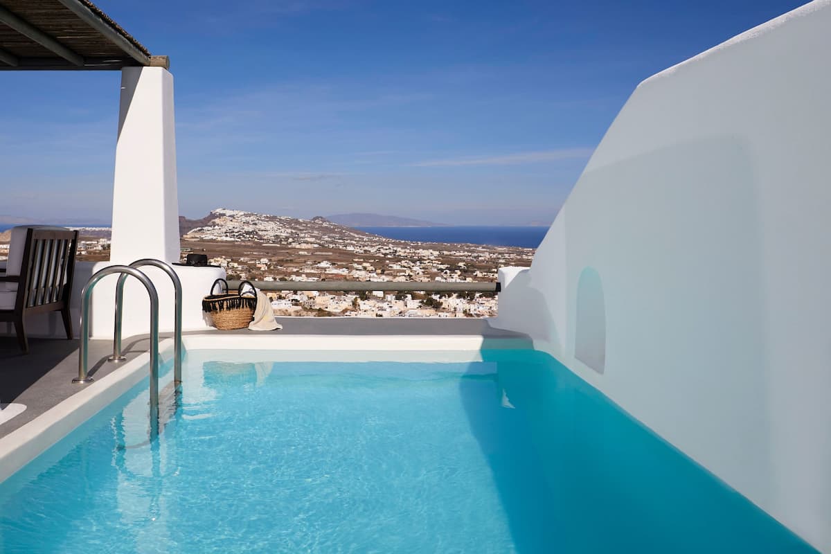 A pool with a view of a coastal town, a white wall, and a metal railing.