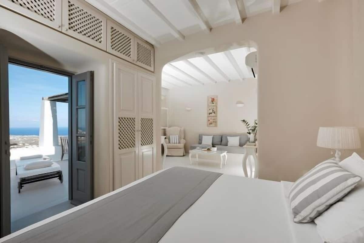 A bedroom with a bed, a sofa, a chair, and a view of the sea.