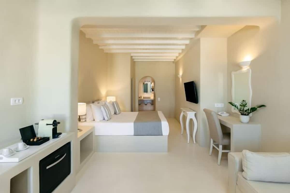 A hotel room with a bed, desk, chair, TV, and a small table with a plant.