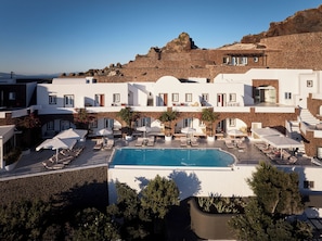 A hotel with a pool, outdoor seating, and a view of the surrounding landscape. - San Antonio (Santorini)