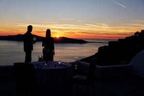 A table set for two with a candle and a glass, overlooking a sunset over water. - San Antonio (Santorini)