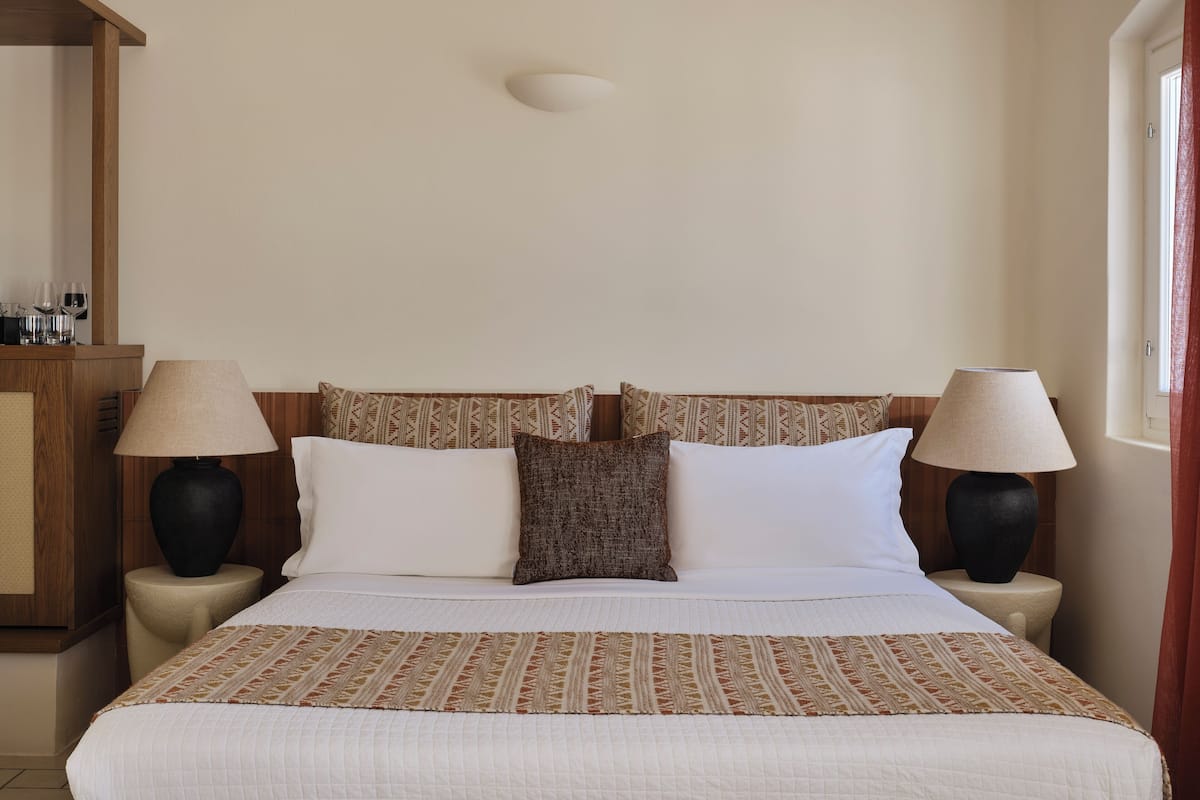 Habitación de hotel ordenada con una cama, dos mesitas de noche, una lámpara y un aplique de pared.