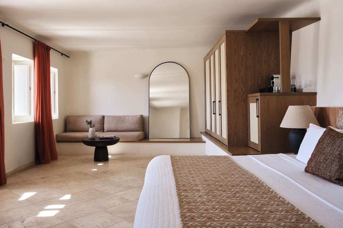 Una habitación de hotel moderna con una cama grande, un sofá, una mesita y un armario.
