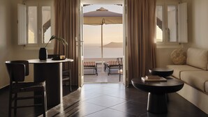 A room with a view of the sea, a dining area with chairs and a table, and a sofa. - San Antonio (Santorini)
