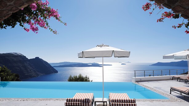 A pool area with a clear view of the sea and mountains, a brick archway, and lounge chairs. - San Antonio (Santorini)