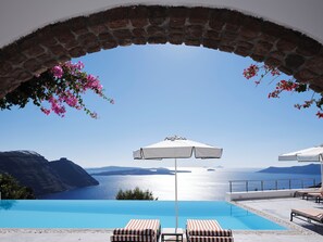 A pool area with a clear view of the sea and mountains, a brick archway, and lounge chairs.