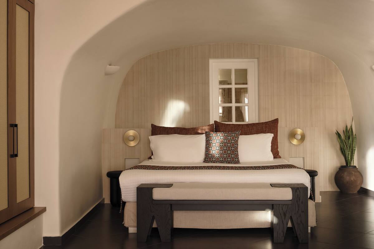 Un dormitorio con cama, mesitas de noche, una ventana y una planta.
