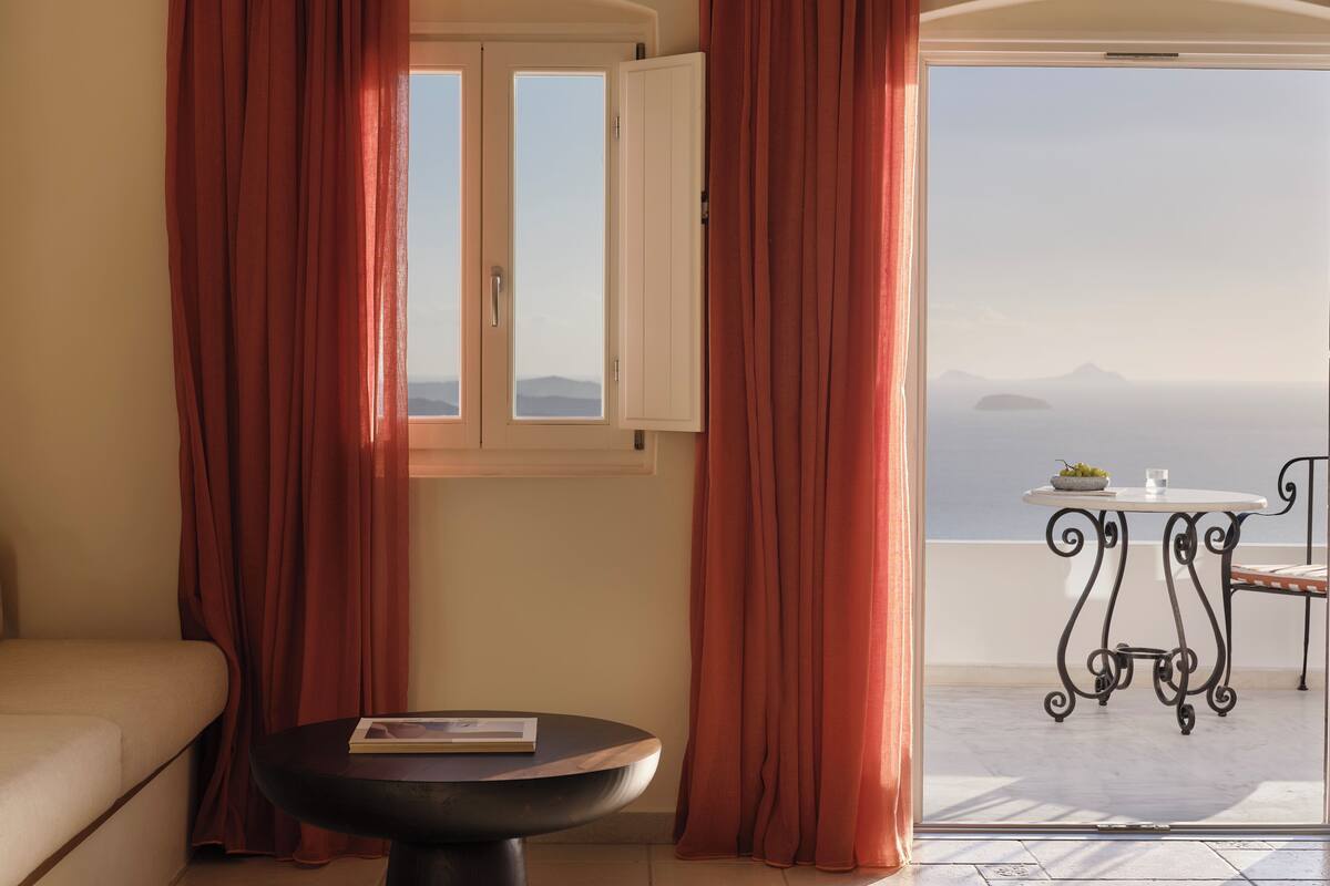 Una habitación con sofá, una mesa con un libro, vista al mar y un balcón con mesa y silla.