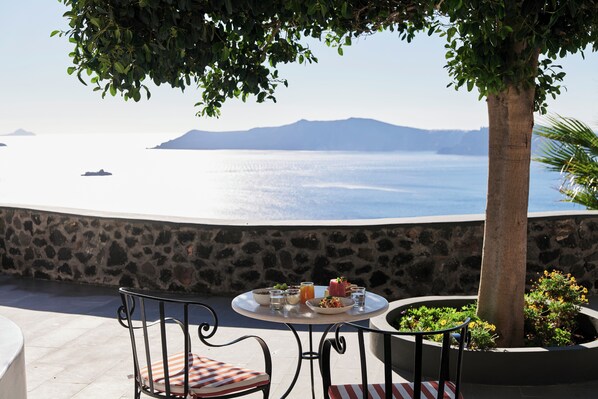 A table with a view of the sea, a stone wall, and a tree.
