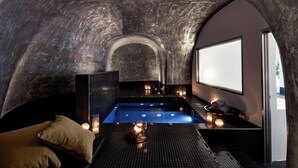 A spa room with a curved ceiling, a small pool, and a seating area with a cushion and candles. - San Antonio (Santorini)