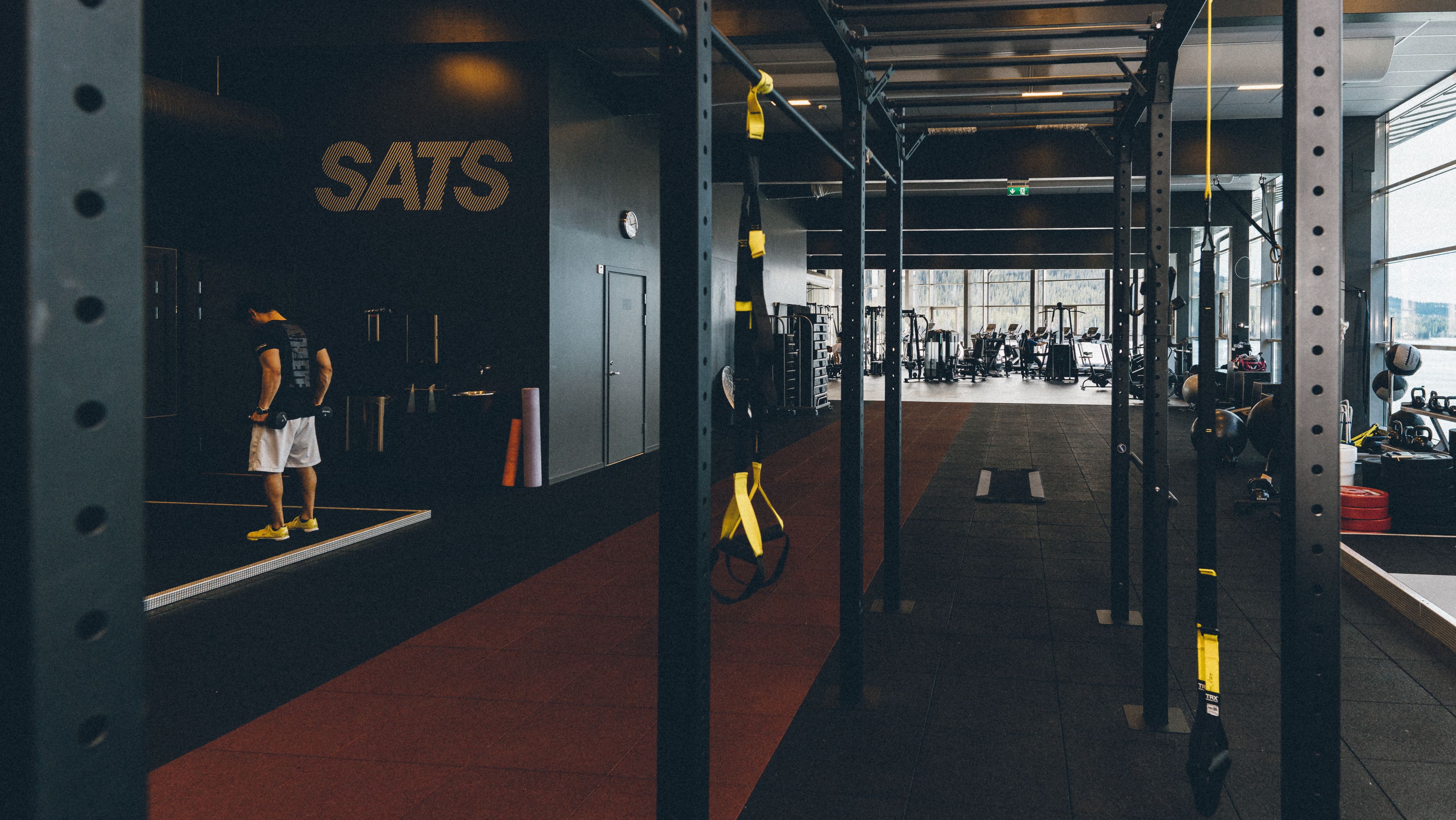 A gym with weightlifting equipment, a person standing on a platform, and a sign that reads "SATS".