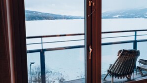 Näkymä huoneesta, jossa on suuri ikkuna, josta avautuu lumipeitteinen maisema, ja ikkunan vieressä on puinen tuoli.