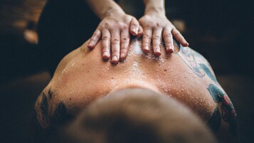 Een close-up van handen die een rugmassage geven, met zichtbare tatoeages.