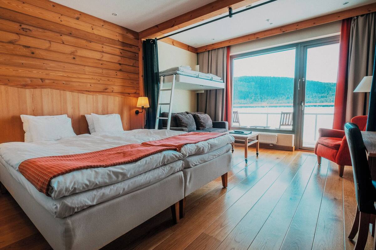 A hotel room with a large bed, two bedside tables with lamps, a sofa, a small table, and a balcony with a view.