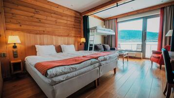 A hotel room with a large bed, two bedside tables with lamps, a sofa, a small table, and a balcony with a view.