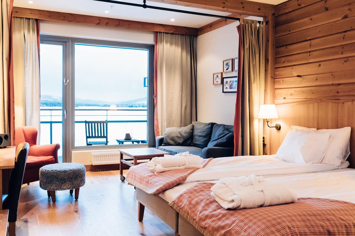 A hotel room with a bed, a chair, a small table, and a view of the outdoors.