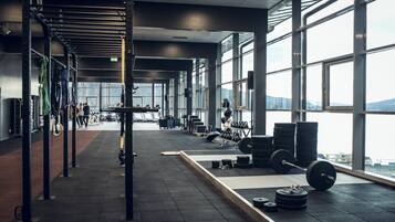 Une salle de sport spacieuse, équipée de matériel de musculation, dotée de grandes fenêtres et offrant une vue sur le paysage urbain.