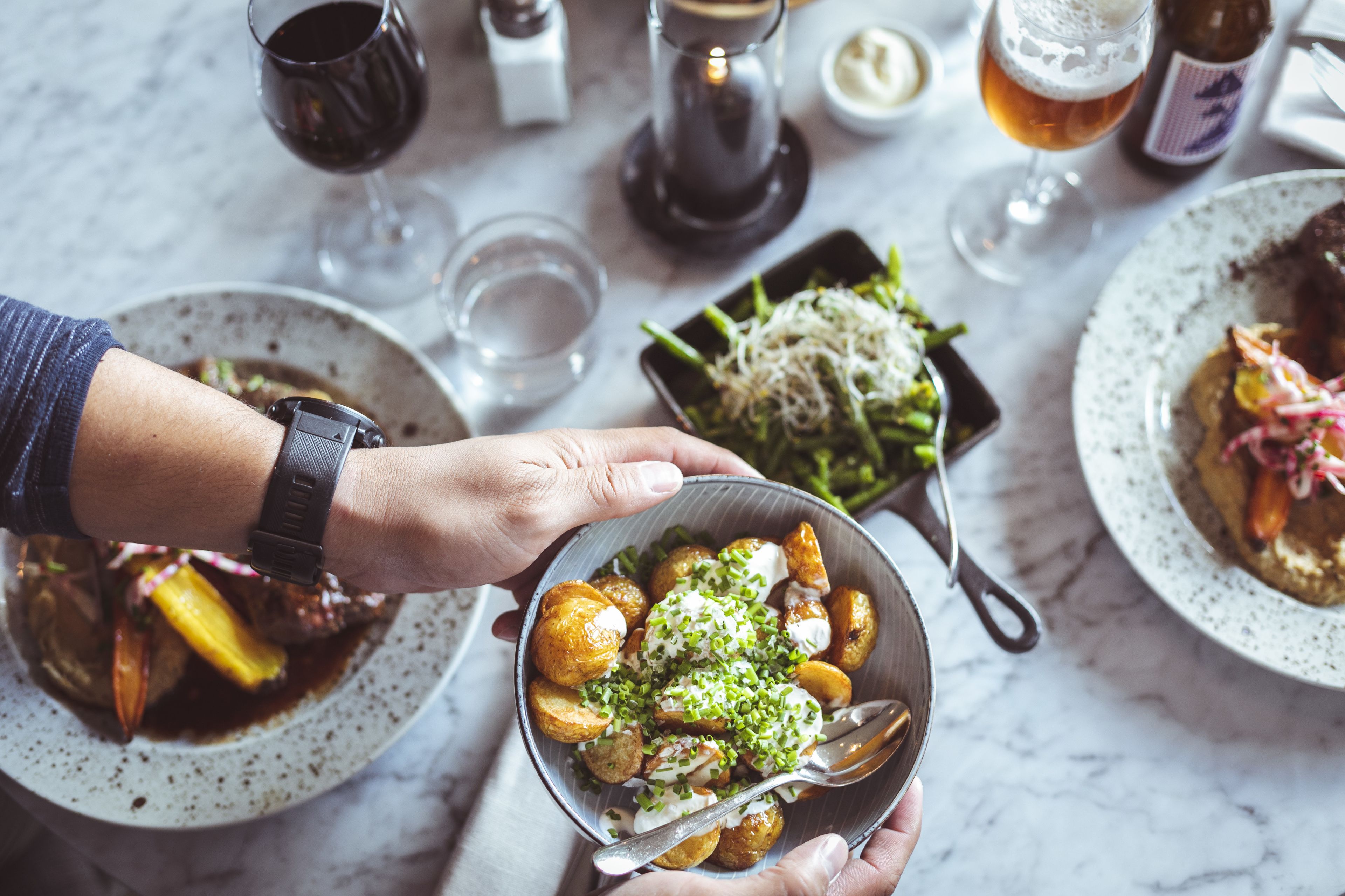 A dining table with various dishes, including a bowl of potatoes with green garnish, a plate with a fish dish, and a glass of beer.
