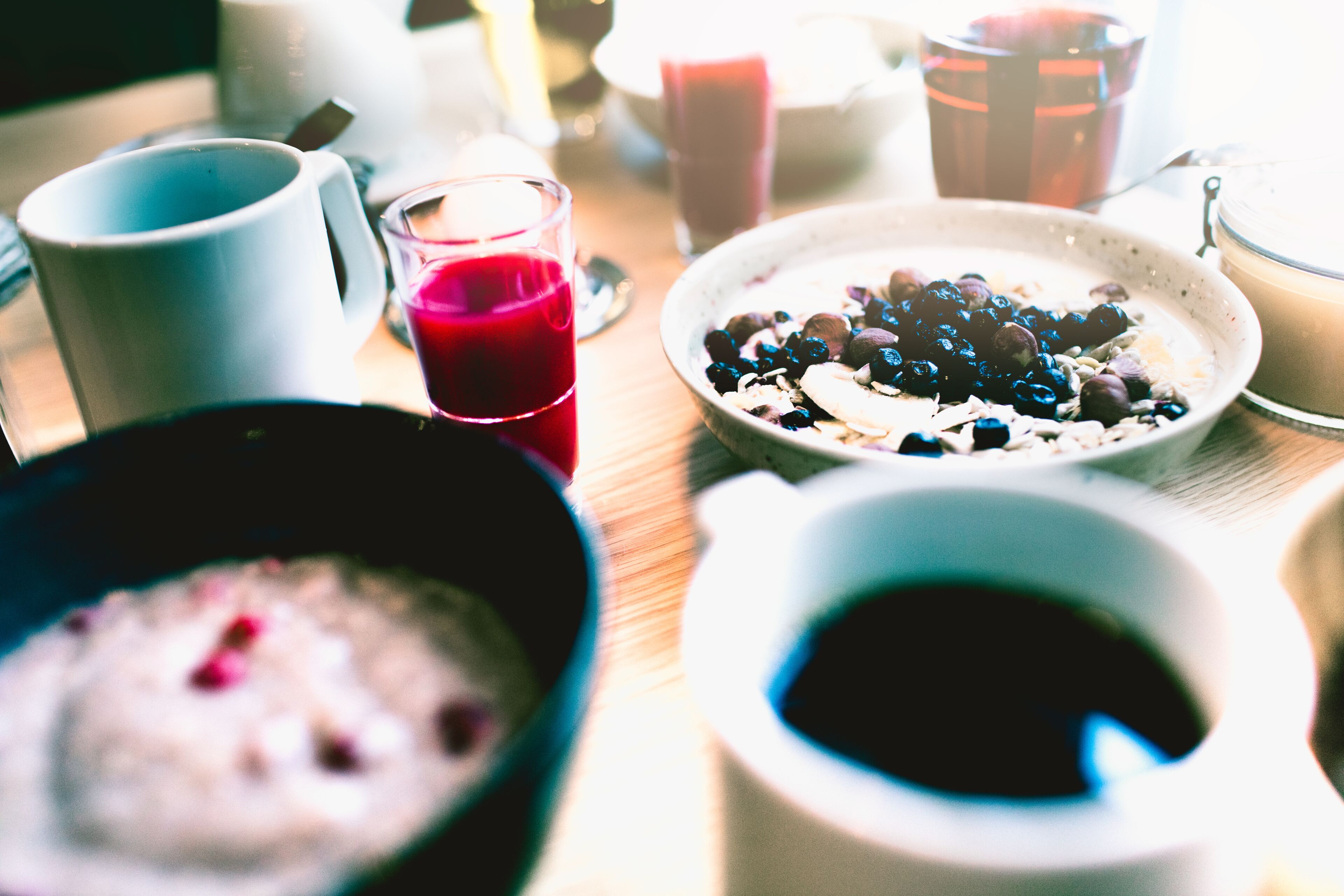 A breakfast table with various dishes including a bowl of oatmeal, a glass of red juice, and a cup of coffee.