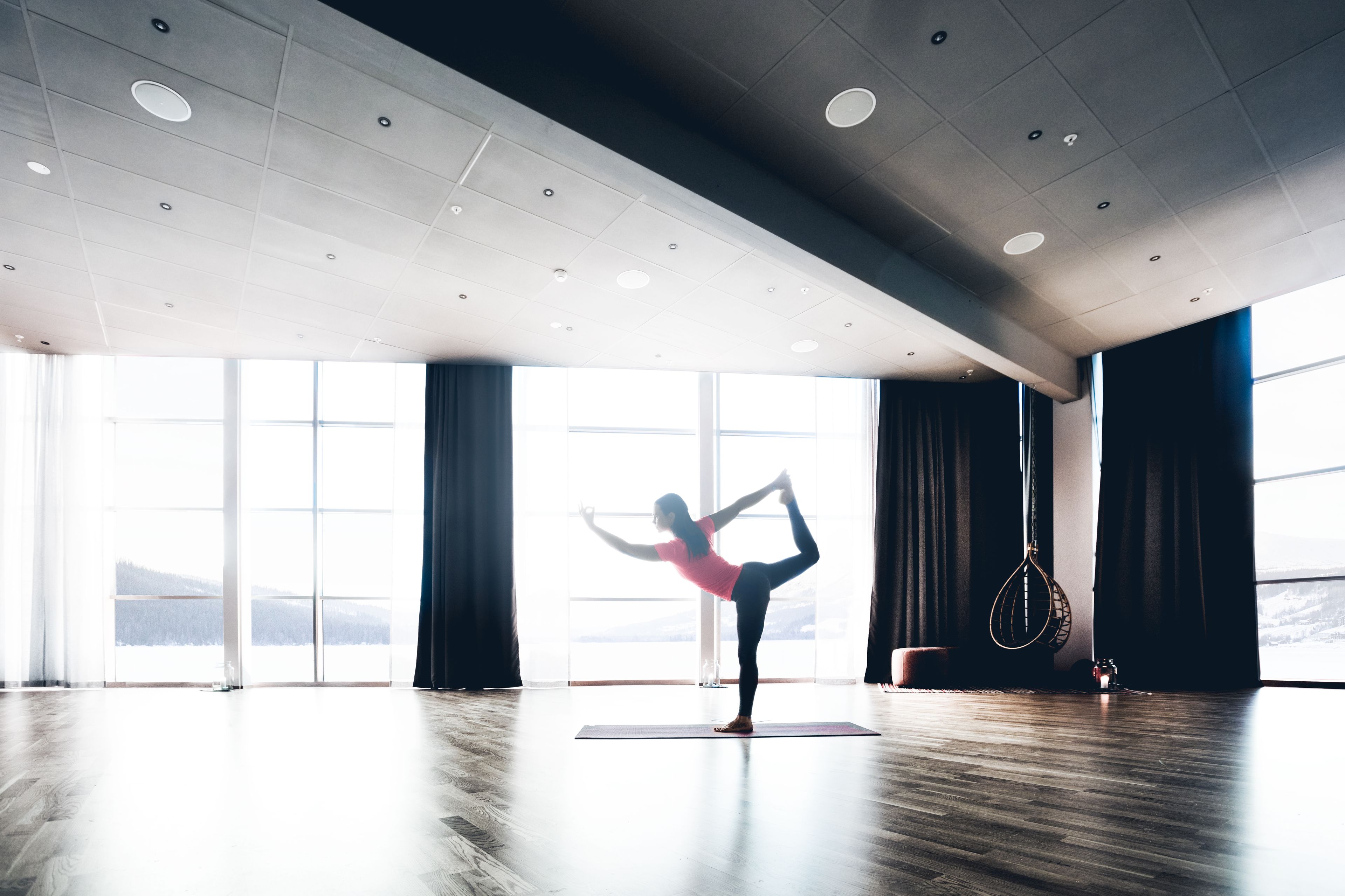 Una habitación amplia con ventanas grandes, suelo de madera y una esterilla de yoga.