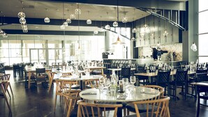 Tilava ravintola, jossa on useita pöytiä ja tuoleja, suuret ikkunat ja katosta roikkuvia, pallomaisia valaisimia.