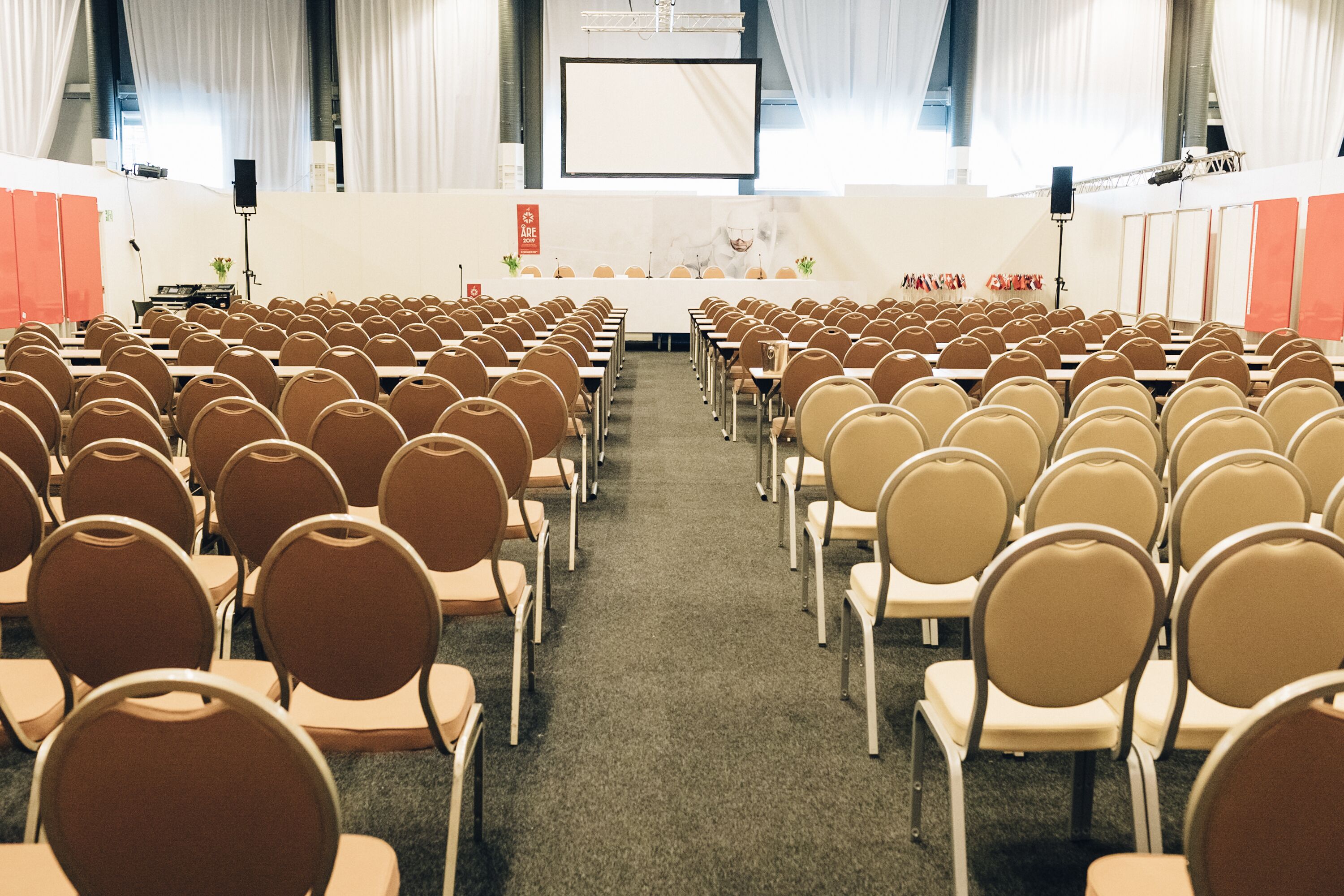 A conference room with rows of chairs facing a stage with a podium and a screen.