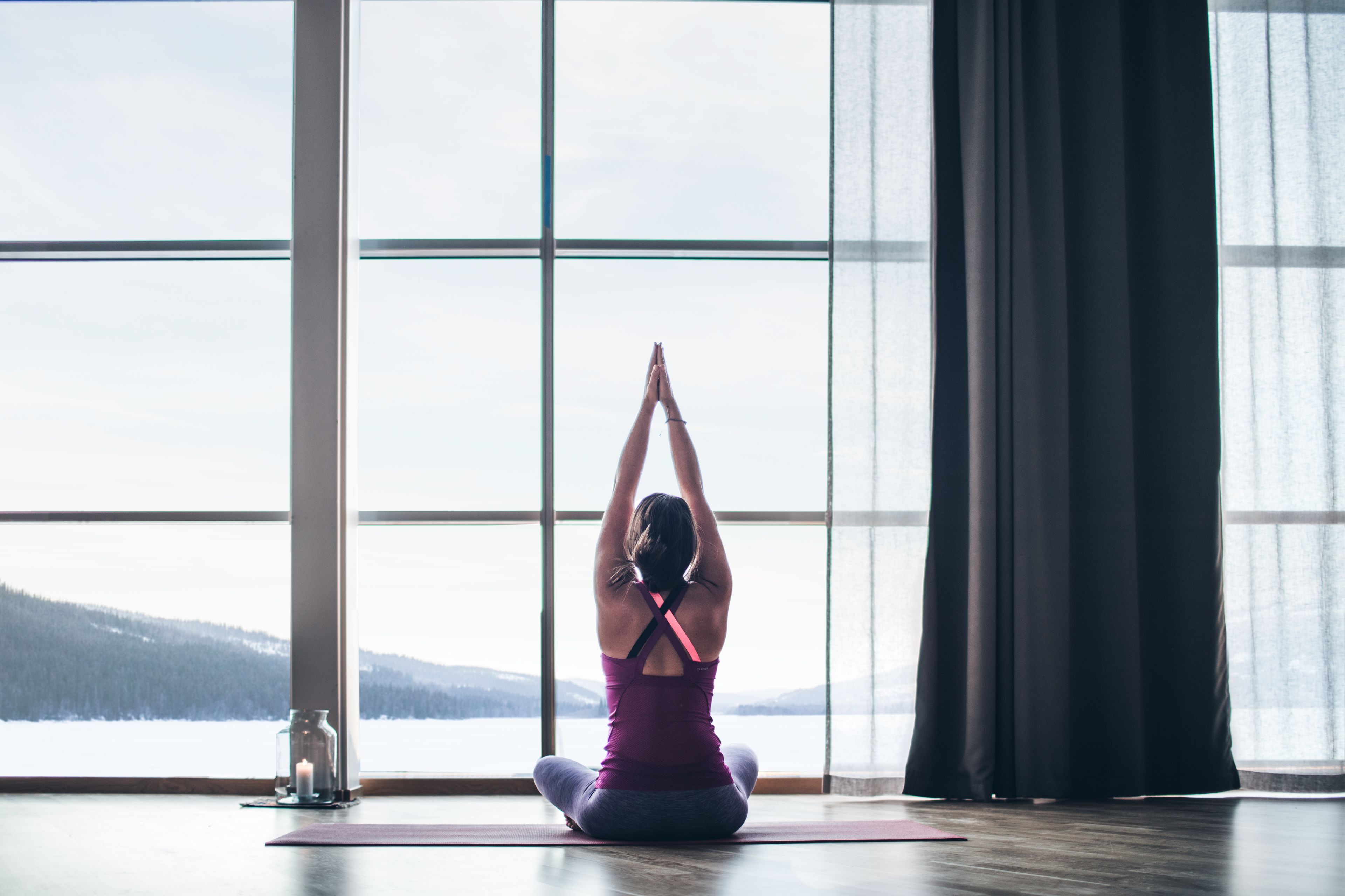 Une personne assise sur un tapis de yoga dans une pièce dotée de grandes fenêtres, offrant une vue sur un paysage enneigé.