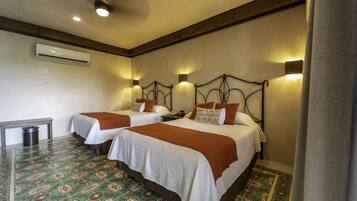A hotel room with two beds, a ceiling fan, an air conditioning unit, and patterned floor tiles.