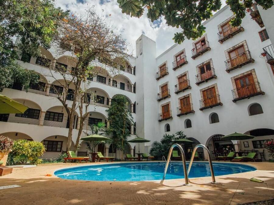 Un patio con piscina, rodeado de edificios blancos con balcones y ventanas arqueadas.