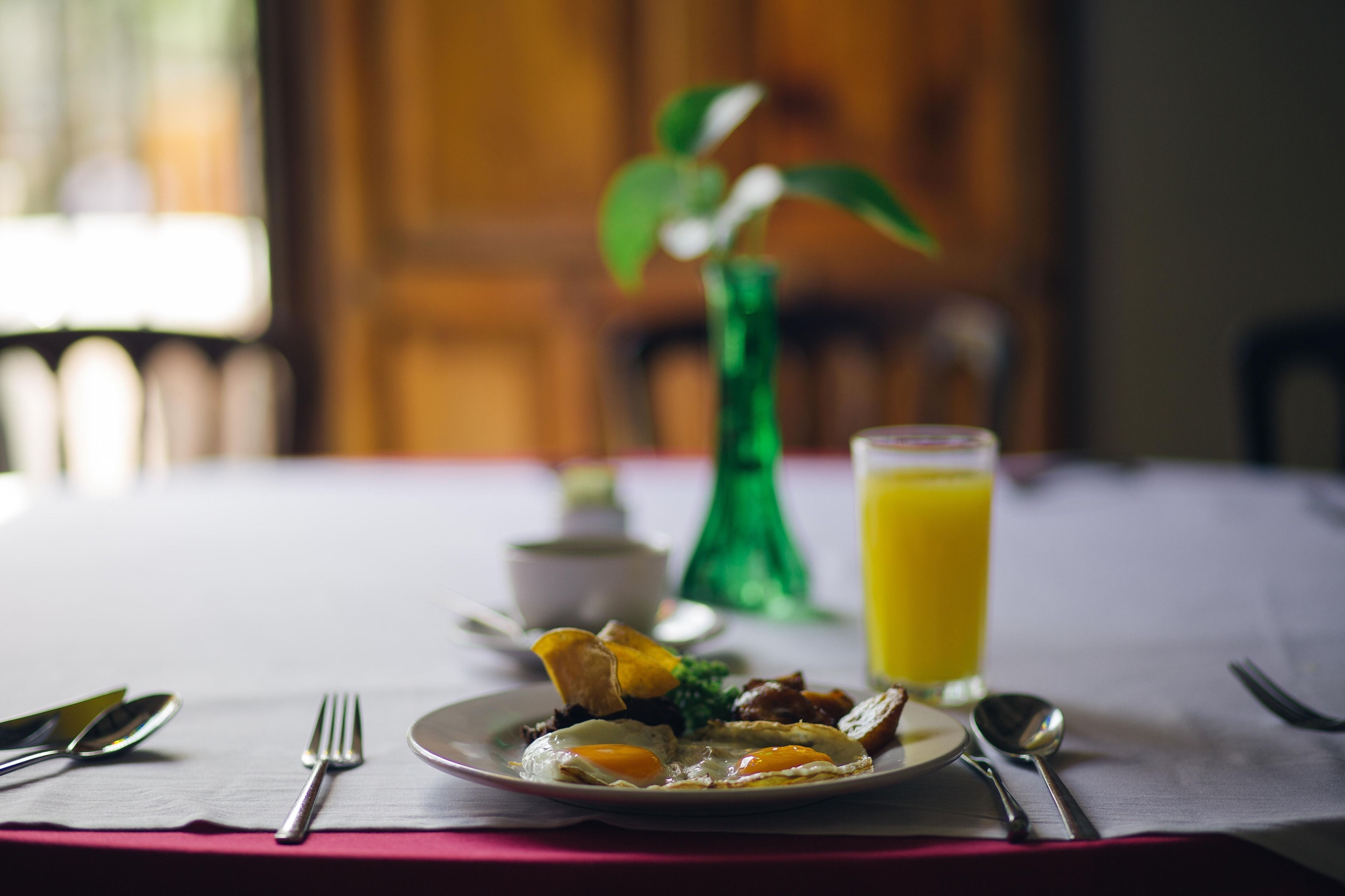 A breakfast setting with a plate of food, a glass of orange juice, and a green vase with a plant.