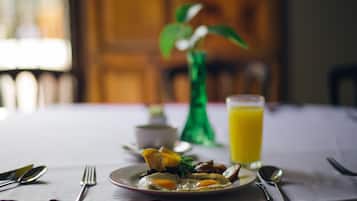 A breakfast setting with a plate of food, a glass of orange juice, and a green vase with a plant.