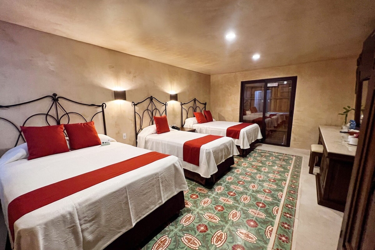 Une chambre d’hôtel avec trois lits, chacun recouvert d’une courtepointe rouge et blanche, et un tapis à motifs verts.