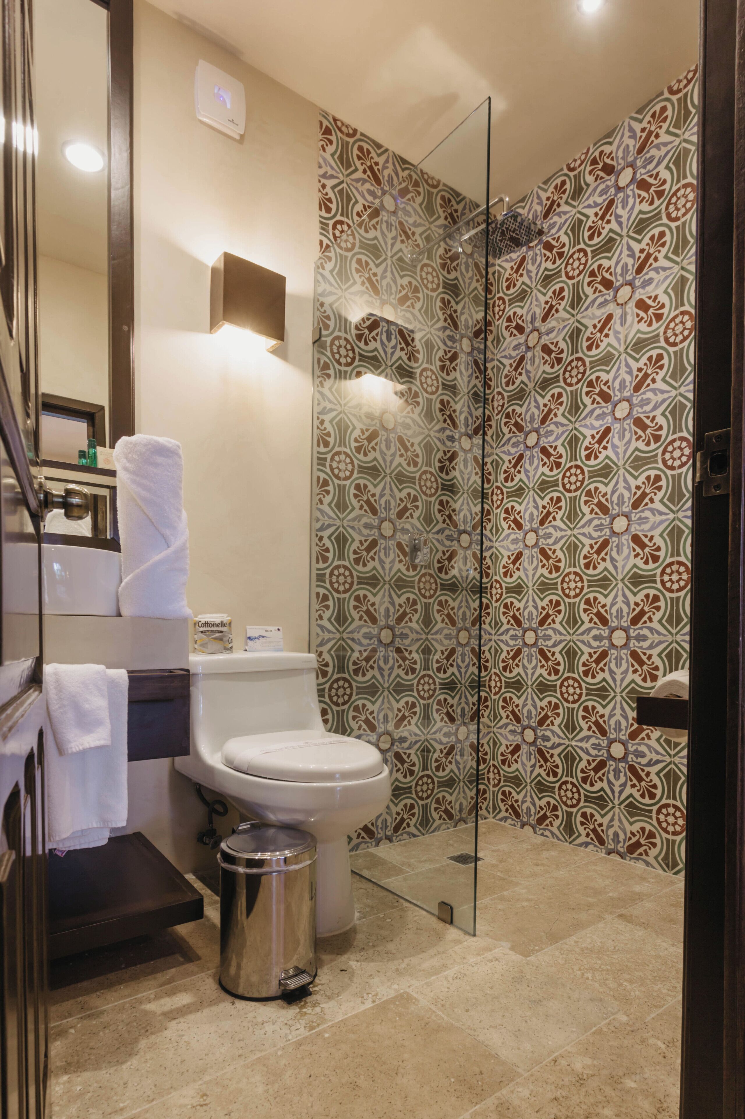 A bathroom with a toilet, a glass shower enclosure, a trash can, and a mirror.