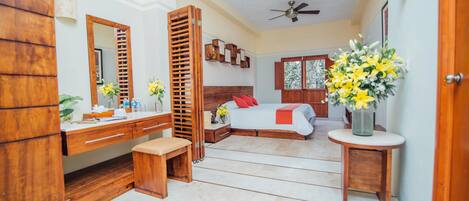 A bedroom with a wooden dresser, a bedside table, a bed with red pillows, and a vase of yellow flowers.