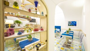 Una habitación con separador de vidrio, estantes con adornos, una mesa con mantel azul y un piso de baldosas con estampado floral.