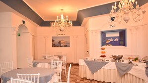 A dining area with white chairs and tables, a chandelier, and a framed picture on the wall. - Hotel Miravalle (Naples)