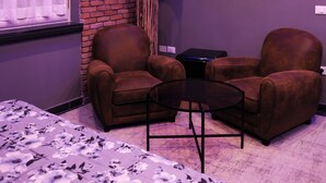 A modern room with a brick accent wall, a flat-screen TV, two brown armchairs, a small round table, and a bed with a floral bedspread. - Hotel Miravalle (Naples)